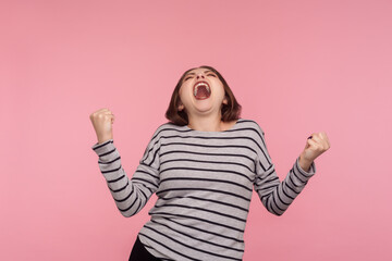 Triumphal victory! Portrait of extremely happy, overjoyed woman in striped sweatshirt yelling for...