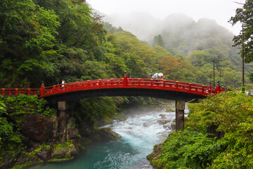 People with umbrellas over red bridge Shinkyo crossing Daiya river. Rainy day, magical and mysterious atmosphere. Beginning of autumn, moth of October. Nikko, Japan, Asia. Horizontal picture