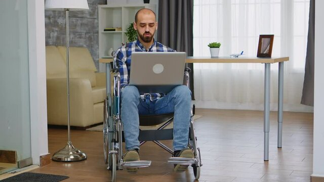 Businessman in wheelchair waving during a video call while working from home. Handicapped invalid paralysed freelancer, immobilized entrepreneur working from home, ilness and disability