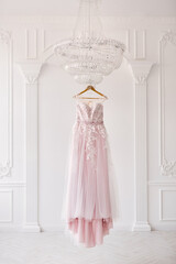 Rich pink wedding dress hangs on a chandelier in a white room