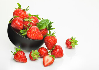 Fresh raw organic strawberries in black ceramic bowl plate on white background with berries next to it.