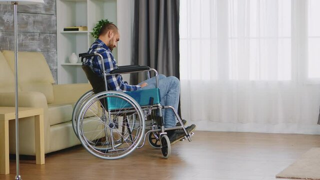 Lonely man in wheelchair with walking disability in living room. Handicapped invalid paralysed person, alone at home, depression and health problems, pensive, sad and unhappy man