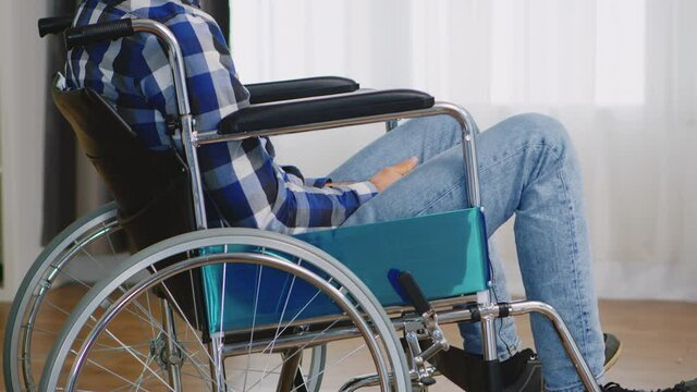 Paralyzed young man sitting on wheelchair in living room. Handicapped invalid paralysed person, alone at home, depression and health problems, pensive, sad and unhappy man