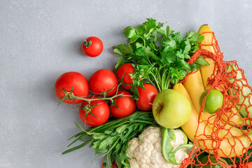 Vegetables and fruits in an eco bag on a gray background, top view.