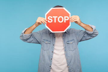 Portrait of anonymous man in worker denim shirt covering face with Stop road traffic sign as symbol...