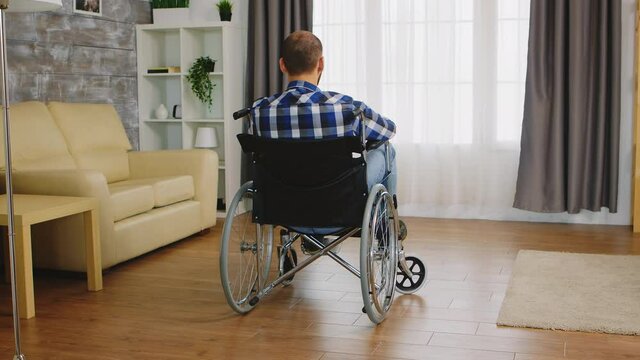 Back view of man with walking disability sitting on wheelchair. Handicapped invalid paralysed person, alone at home, depression and health problems, pensive, sad and unhappy man
