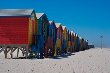 Naklejka premium Colorful beach houses and blue sky in Muizenberg Beach in South Africa. Multi-colored beach huts in Western Cape