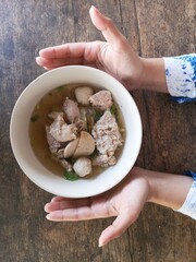 two hands hold the bowl of clear soup, pork, vegetable, pork ball, thai food style call 