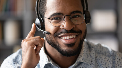 Close up african man wear headset with microphone smile look at camera. Internet selling worker, tutor provide lecture for trainee distantly, company representative contact with client online concept - obrazy, fototapety, plakaty
