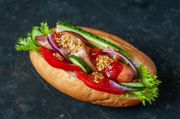 Hot dog against a dark background. Fresh tomatoes. cucumbers, sausages, mustard, lettuce and bacon.