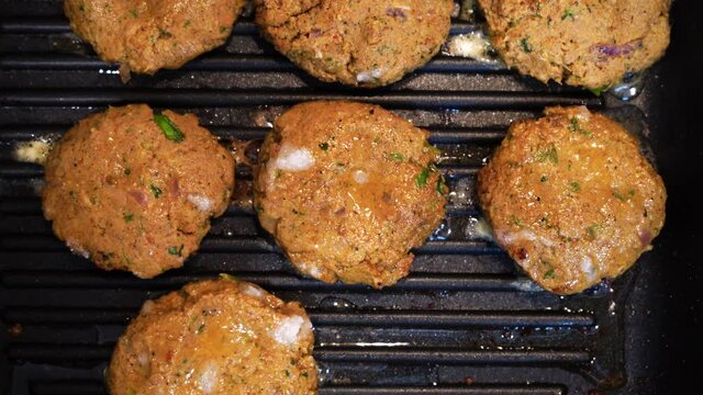 Shallow depth of feild shot mince meat mutton patties keema roasting on a pan with oil bubbling out as they get charred