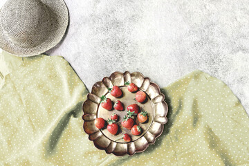 Retro summer theme with polka dot green dress, straw hat and strawberry in vintage brass dish.