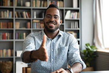 African man HR agent sit at workplace desk stretch hand for handshake greeting new applicant start...