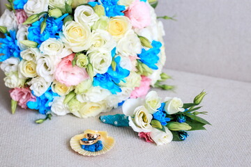 gold wedding rings lie next to the boutonniere and wedding bouquet. Wedding bouquet with white eustoms and blue chrysanthemums