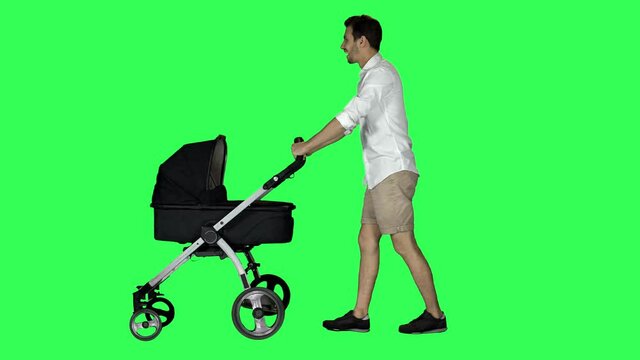Casual dad walking with a stroller, looking around and at his baby, smiling and waving hello, over green screen.