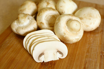 Sliced slices on the background of whole mushrooms on a wooden board in the kitchen. A dish of champignons. Useful vegetarian menu.