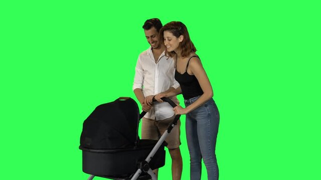 Young parents pushing a stroller, smiling, looking to the camera over green screen