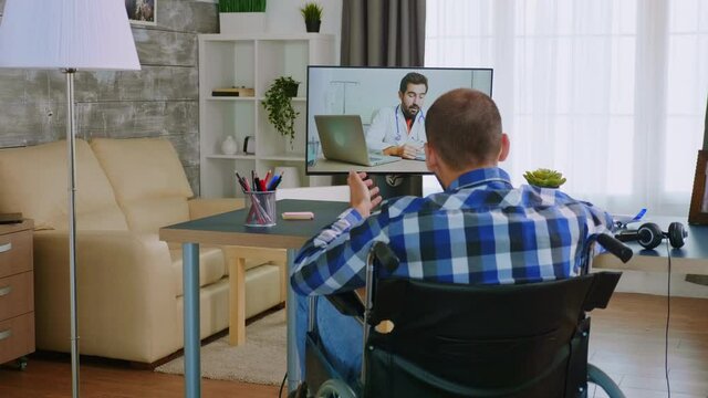 Disabled young man in wheelchair during a video call with his doctor. Handicapped invalid paralysed person, alone at home, depression and health problems, pensive, sad and unhappy man
