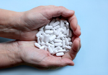 White pills in hands, blue background