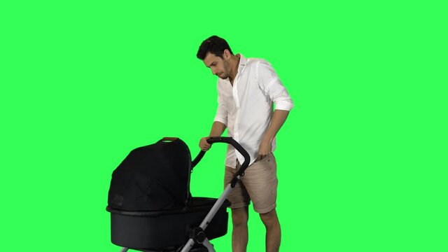 Relaxed dad pushing a stroller, smiling, taking a photo of his baby, over green screen.