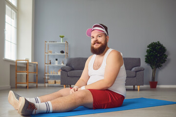 Funny red fat man doing exercises on the floor smiling while sitting on the floor at home.