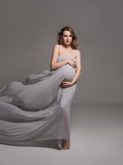 Pregnant woman wrapped in veil holding her belly with arms.Fashion portrait of happy pregnant woman..Pregnancy, maternity, preparation and expectation concept. Close-up, copy space.