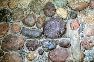 Stone wall as a background. Masonry made of natural, polished by the sea, cobblestones. Multi-colored, natural stones in the interior.