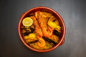 Seafood paella in ceramic bowl on dark wooden background. Rice with seafood.