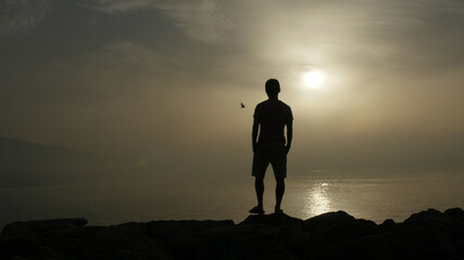 Silhouette of young man looks at sunrise and reflection of sun on sea water in Marbella area, Spain