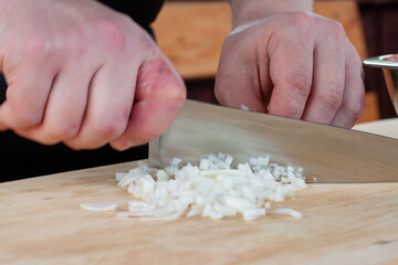 the chef cuts the onion to fry on the Board. hands with a knife in the frame.