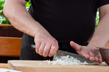 the chef cuts the onion to fry on the Board. hands with a knife in the frame.