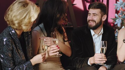 In front of the camera charismatic group of students celebrating Christmas party while sitting on the sofa they socializing and drinking some sparkling wine