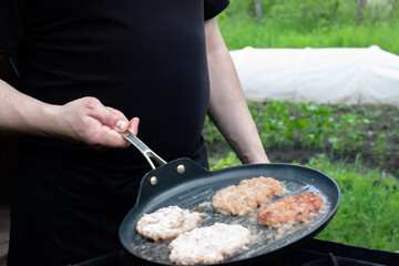 the cook roasts the cutlets in a pan over the fire. food on the grill in nature. picnic.