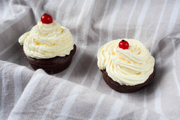 two gluten free rice and corn flour chocolate cupcakes with cream cheese on a gray and white surface with red currant berries prepared at home