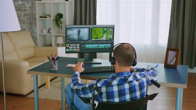 Invalid man in wheelchair editing a video using post production software wearing headphones. Handicapped invalid paralysed freelancer, immobilized entrepreneur working from home, ilness and disability