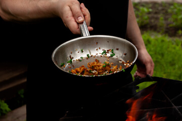 the cook roasts mushrooms with onions and herbs on the fire. chanterelles