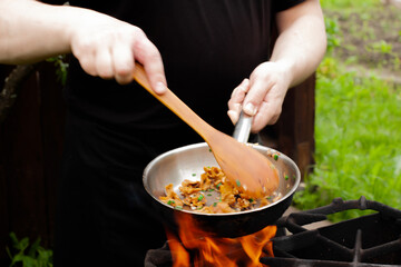 the cook roasts mushrooms with onions and herbs on the fire. chanterelles