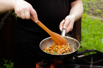the cook roasts mushrooms with onions and herbs on the fire. chanterelles