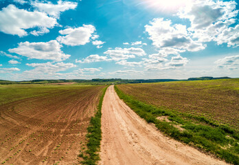 Rural landscape with beautiful sky, farmland, aerial view. View of dirt road through the plowed field in spring
