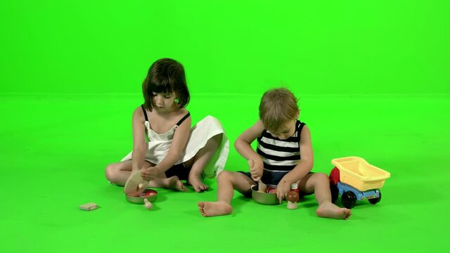 Playing together with kitchen toys by a brother and a sister, over green screen.