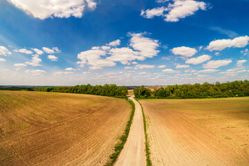 Fototapeta premium Rural landscape with beautiful sky, farmland, aerial view. View of dirt road through the plowed field in spring