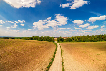 Rural landscape with beautiful sky, farmland, aerial view. View of dirt road through the plowed field in spring
