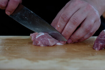 cutting meat into pieces with a knife on a wooden Board. the cook cuts the meat.