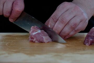 cutting meat into pieces with a knife on a wooden Board. the cook cuts the meat.