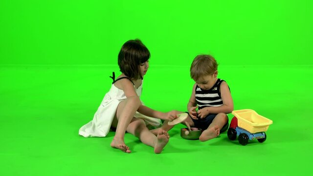 Cooking together with kitchen toys by a brother and a sister, over green screen.