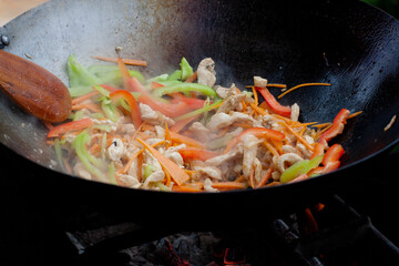 cook with a wooden spatula stir onions, carrots and chicken in a wok on the fire