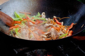 cook with a wooden spatula stir onions, carrots and chicken in a wok on the fire