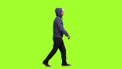 Hooded man walks on green screen background, Side view Chroma key