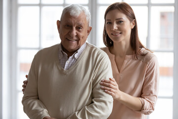 Fototapeta na wymiar Head shot portrait smiling older father with grownup daughter looking at camera, happy mature man and young beautiful woman standing at home, posing for photo together, two generations concept
