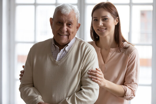 Head shot portrait smiling older father with grownup daughter looking at camera, happy mature man and young beautiful woman standing at home, posing for photo together, two generations concept